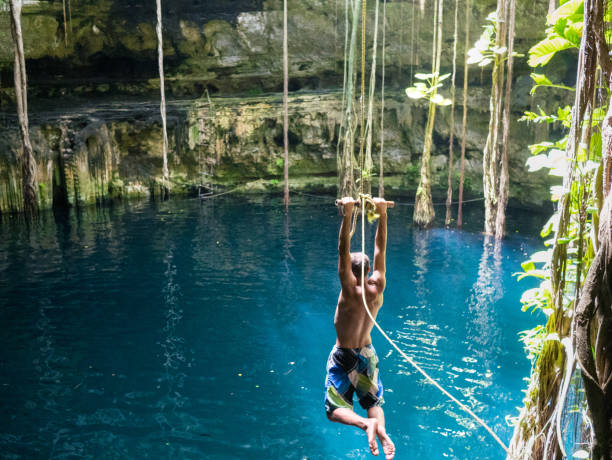 Young man using a rope swing to jumpp into Cenote sink hole Oxman in Yucatan, Mexico, 2017