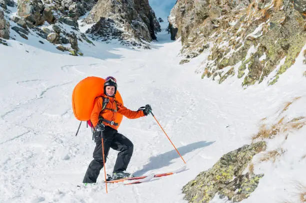 Portrait of a smiling happy freeride backcountry skier with an opened avalanche dowel abs in a backpack. Portrait on a background of a high-mountainous rocky couloir. The concept of freeride backcountry skiing and extreme winter sports