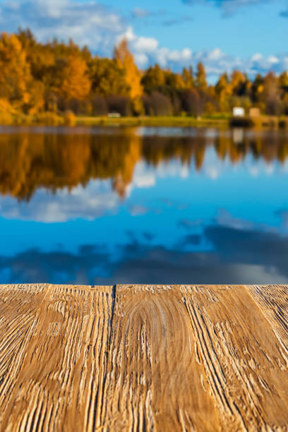 istock Empty rustic wood table top on  blurred colorful autumn landscape background with fall forest and blue sky with cloudscape reflection on the lake. Can montage or display your products 914563186