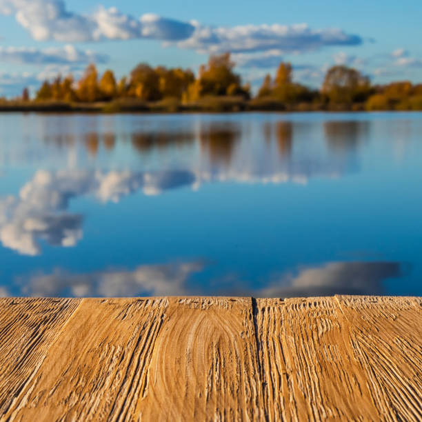 istock Empty rustic wood table top on  blurred colorful autumn landscape background with fall forest and blue sky with cloudscape reflection on the lake. Can montage or display your products 914563218