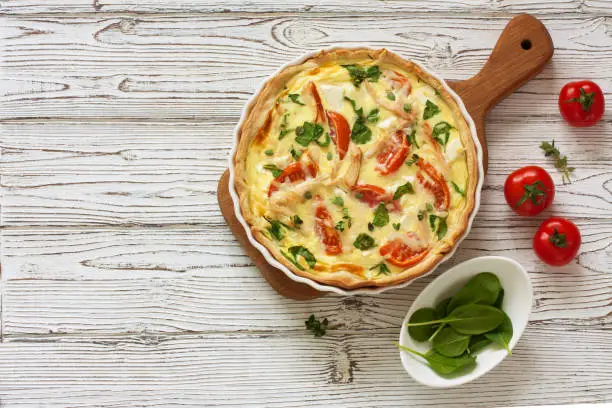 Chicken, spinach and tomatoes pie( quiche) on a white wood background. Top view