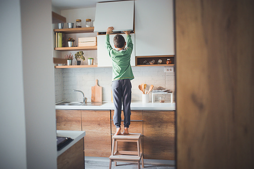 Young boy, home alone, trying to reach for something from a kitchen cabinet