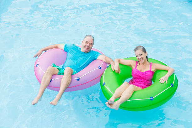 istock Mature couple holding hands floating on inflatable rings 914621862