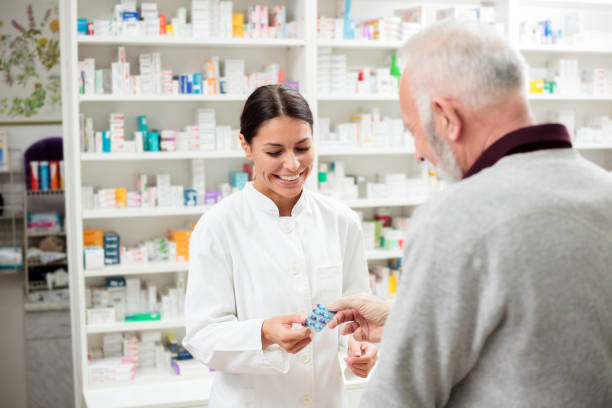 Female pharmacist giving medications to senior customer Medicine, pharmaceutics, health care and people concept - Happy female pharmacist giving medications to senior male customer chemist photos stock pictures, royalty-free photos & images