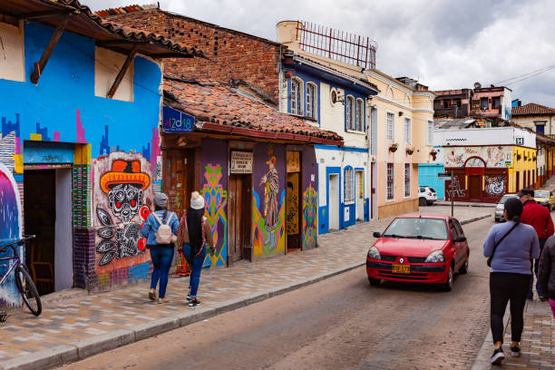 bogotá, colombia - coche coches y gente a pie a través de las coloridas calles del histórico distrito la candelaria en la ciudad capital. - graffiti paintings men walking fotografías e imágenes de stock