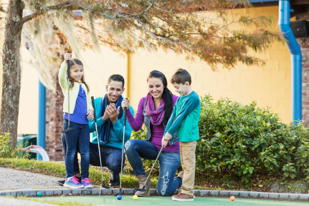 family playing miniature golf, boy putting - golf four people young adult playing imagens e fotografias de stock