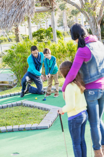 family playing miniature golf, dad helping son - golf four people young adult playing imagens e fotografias de stock