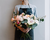 Young florist woman holding freshly made blossoming flower bouquet on the grey wall background.