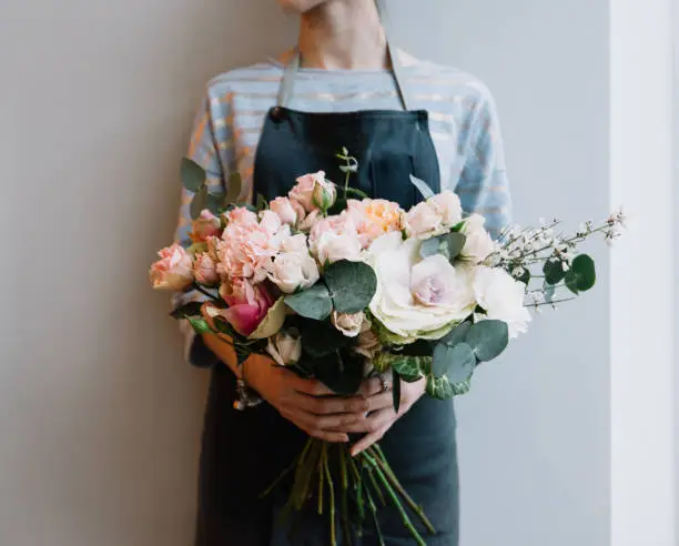 Photo of Young florist woman holding freshly made blossoming flower bouquet on the grey wall background.