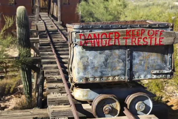 Isolated Mine Cart with Red Paint Danger Trestle Sign on Old Rusted Rail Tracks next to Saguaro Cactus in Arizona Desert near Phoenix
