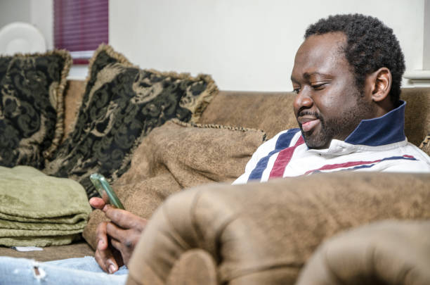 istock Young black man using his cell phone while sitting in his couch at home 914662812