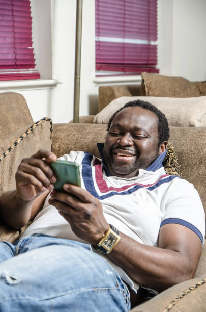 istock Young black man using his cell phone while lying in his couch at home 914666036