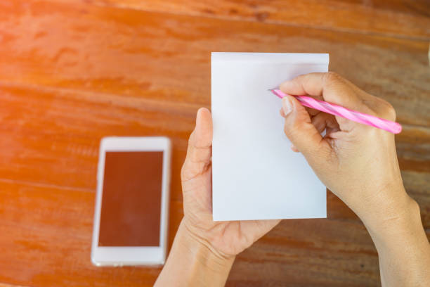 Closeup of business woman hand writing note and using mobile phone