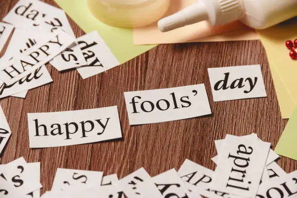 Photo of Happy Fools Day phrase on wooden background