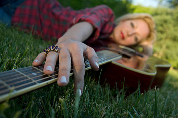Portrait of a beautiful smiling blonde girl in a straw hat outdoors playing guitar