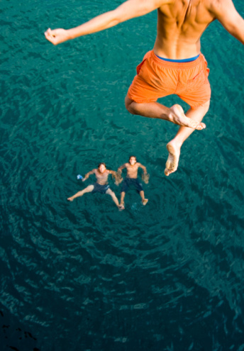Young adventurous couple cliff jumping into beautiful sea.