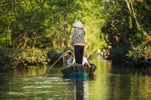 My Tho, Vietnam - January 04, 2016: A woman wearing a conical hat rowing a boat with tourists on a river on the Mekong delta area near My Tho, Vietnam.