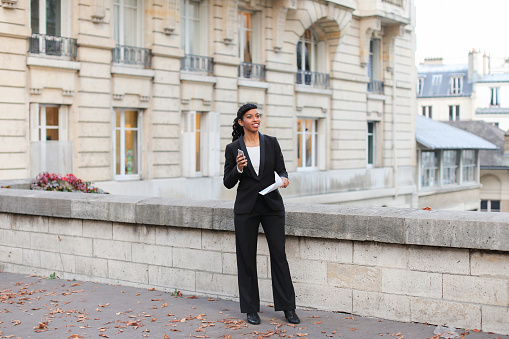 Programmer got well-paid job in big IT-company. Smiling female with summary in hands dancing incendiary. Young black-haired woman wearing strict black suit and white blouse for interview. Concept of success, international cooperation, beginning of working path.