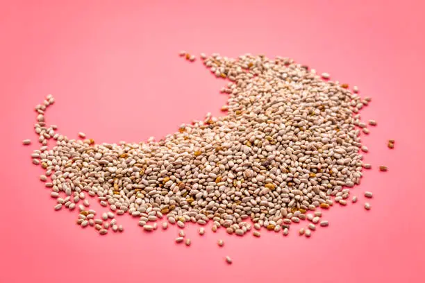a small pile  of organic white chia seeds rich in omega-3 fatty acids on a pink background