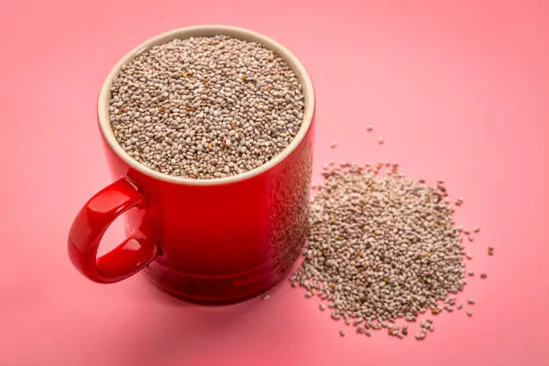 a small coffee cup of organic white chia seeds rich in omega-3 fatty acids against pink background
