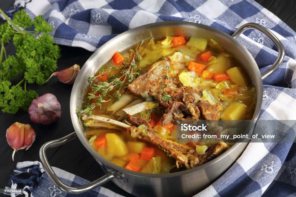 Lamb winter hot Soup with i a pot delicious Icelandic Lamb winter hot Soup with vegetables and spices or kjotsupa in a stainless steel casserole pan on wooden table with kitchen towel, traditional recipe, view from above, close-up Iceland Stock Photo