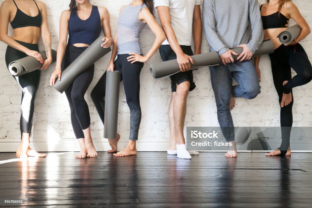 Group of young sporty people standing at wall, close up Group of young sporty people standing at wall. Students taking a rest from fitness activity, time to recover strength, waiting for a lesson to start in loft studio, close up. Healthy lifestyle concept Yoga Stock Photo