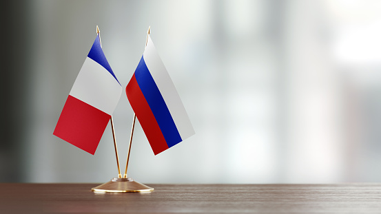 French and Russian flag pair on desk over defocused background. Horizontal composition with copy space and selective focus.