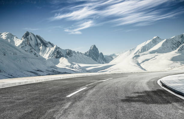 strada asfaltata vuota che porta verso montagne innevate - snowcapped mountain mountain range snow foto e immagini stock