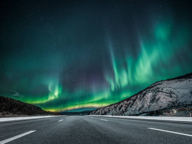 aurora borealis over asphalt road in canada - natural landmark winter season mountain peak imagens e fotografias de stock