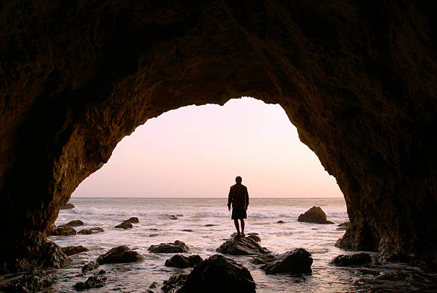 silhouette mann stehend in der see-höhle bei sonnenuntergang - horizon over water malibu california usa stock-fotos und bilder