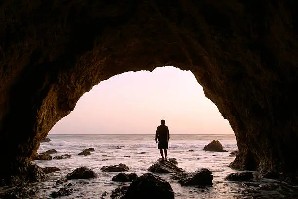 Photo of silhouette man standing in sea cave at sunset