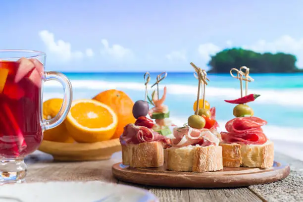 Set of Spanish tapas served on a sliced baguette with sangria on wooden table against the sea