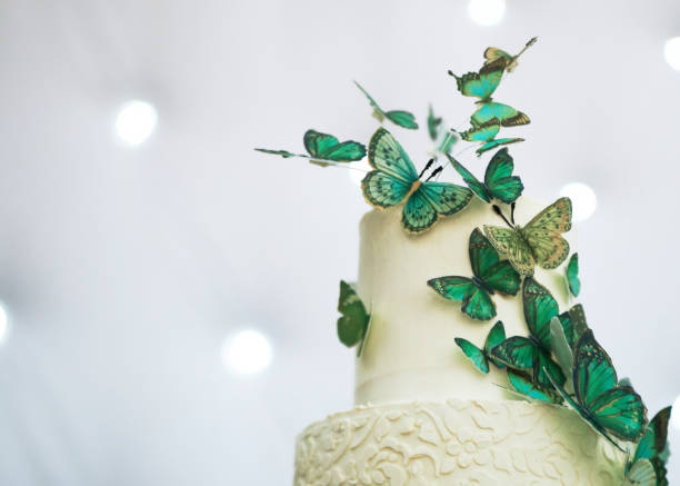 Two-tier wedding cake is decorated with green butterflies on glasses table.