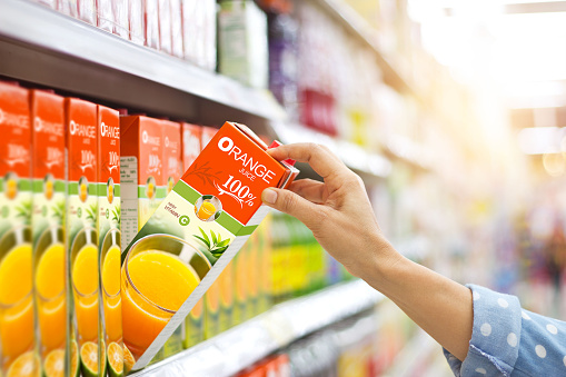 Woman hand choosing to buy orange juice on shelves in supermarket