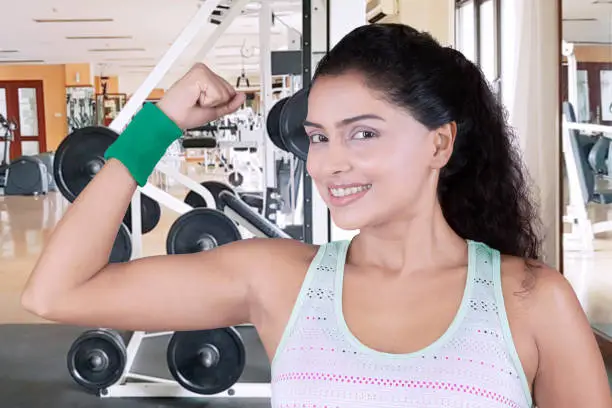 Image of young Indian woman smiling at the camera while showing her beautiful arm in the fitness center