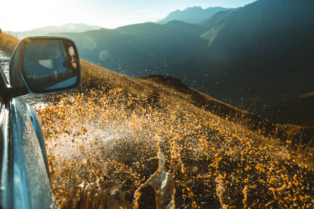 suv-auto fährt durch schlammige pfütze, geländestrecke straße, mit einem big splash, während im hintergrund eine berglandschaft - sports utility vehicle 4x4 car mud stock-fotos und bilder