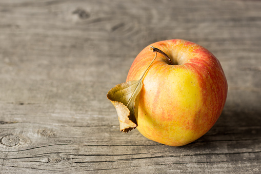 Yellow apple with red sidewalls and a dried leaf on a wooden background. Copy space for text
