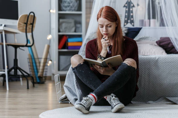 Girl thinking over notebook Cogitative, redhead girl thinking over a notebook while sitting on a floor in her room girl writing in journal stock pictures, royalty-free photos & images