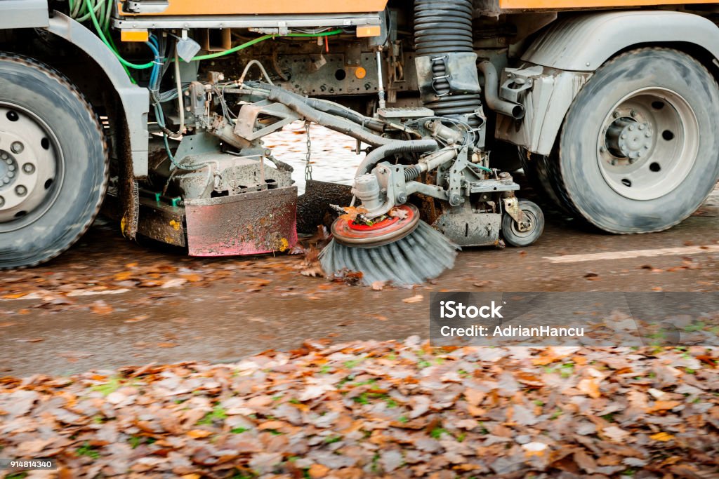Truck sweeper on urban city street cleaning leaves Working orange street sweeper truck on the street working cleaning autumn foliage Road Stock Photo