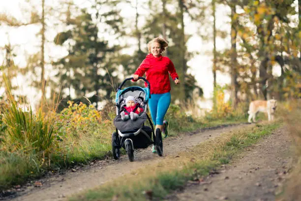 Running mother with child in stroller enjoying motherhood at autumn sunset and mountains landscape. Jogging or power walking woman with pram in woods. Beautiful inspirational mountains landscape.