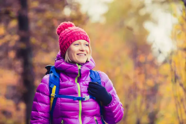 Hiking woman with backpack looking at inspirational autumn golden trees and woods. Fitness travel and healthy lifestyle outdoors in fall season nature. Female backpacker tourist walking in forest.