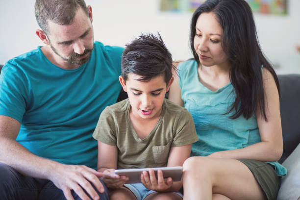istock Mixed race family sitting on sofa looking at son's homework on digital tablet 914827110