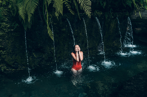 Young Caucasian woman in red swimsuit standing in spring swimming  pool in Bali
