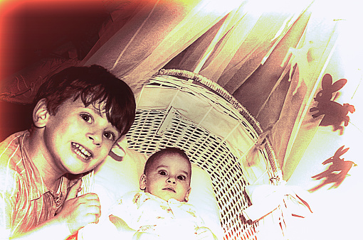 vintage sepia toned photo from the sixties/seventies featuring a boy besides his new baby sister in a cradle