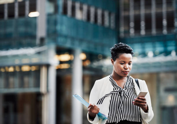 On that go get it grind Shot of a young businesswoman using a mobile phone on the go in the city serious business stock pictures, royalty-free photos & images