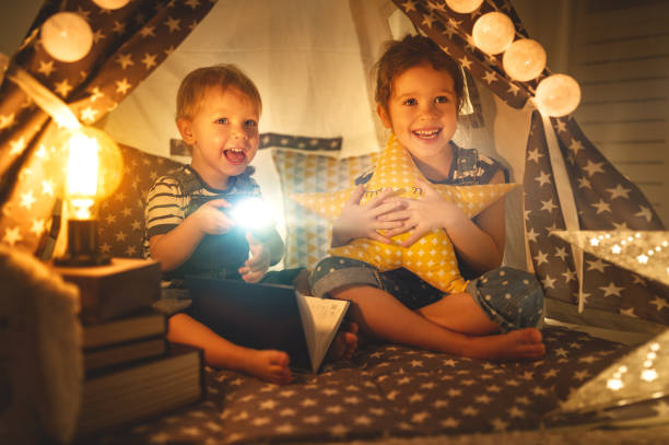 niño niños y niña lectura libro con la linterna en la tienda - child bedtime imagination dark fotografías e imágenes de stock