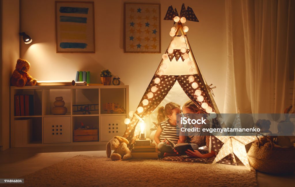 mother and child daughter with a book and a flashlight before going to bed reading and family games in   tent. mother and child daughter with  book and flashlight before going to bed Child Stock Photo