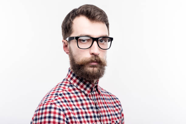 Serious attitude. The portrait of a handsome bearded man in eye glasses standing half-turned and looking at the camera with a serious expression