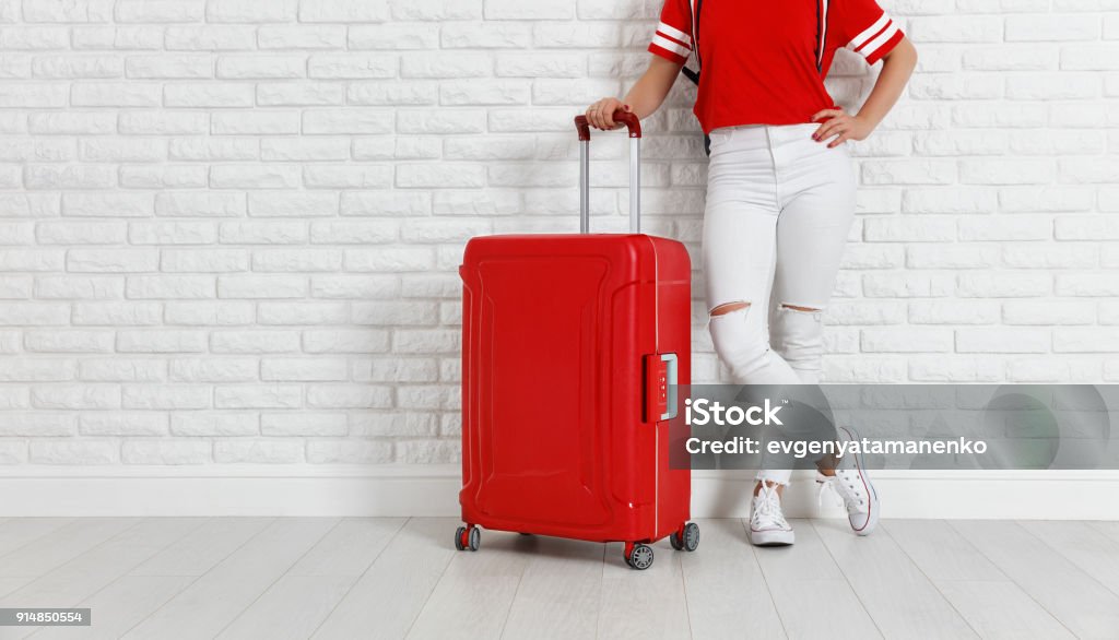 concept travel and tourism. legs of  girl with a red suitcase near white empty brick wall concept travel and tourism. legs of a girl with a red suitcase near  white empty brick wall Red Stock Photo