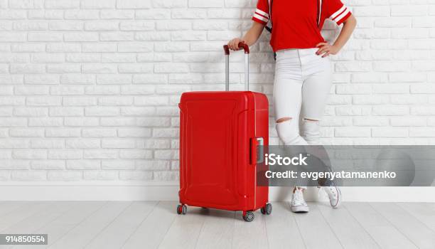 Concept Travel And Tourism Legs Of Girl With A Red Suitcase Near White Empty Brick Wall Stock Photo - Download Image Now